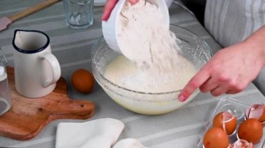 Adding flour and mixing dough in glass bowl. Female hands using hand mixer, cooking sweet dessert