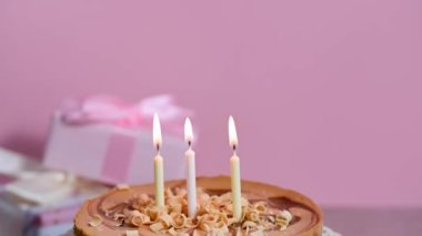 Three burning candles and birthday cheesecake pink background. High quality 4k footage