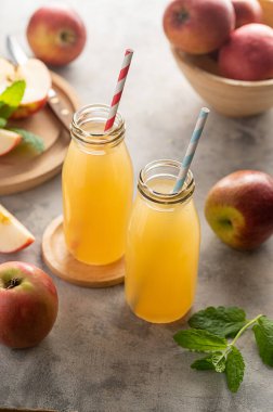 Elma suyu şişeleri, taze kırmızı elmalar, ahşap arka plan.