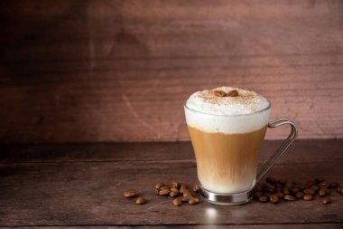Süt köpüklü, ahşap arka planlı ve fotokopi alanından oluşan katmanlı bir bardak kahve..