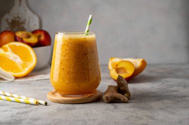 Şeftali, zencefil ve portakaldan yapılmış bir bardak portakallı smoothie.