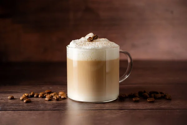 ミルクフォームと層状コーヒードリンクのガラスカップ 木製の背景にコーヒー豆 コピースペース — ストック写真