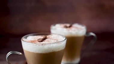Two cups of coffee hot drinks, with milk foam in glass cups, over wooden background.