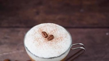 Coffee hot drink with milk foam in glass cup, over wooden background.