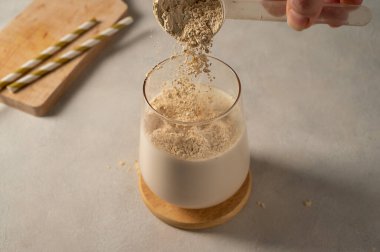 Kepçeden protein tozu dökülüyor, milkshake ile birlikte bardakta.