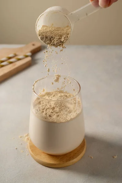 Pouring protein powder from scoop, in glass with milkshake