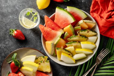 Meyve tabağı, karpuz, ananas, kavun ve çilek. Koyu arkaplan.