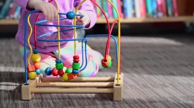 3 yaşında küçük bir kız kütüphanede eğitici, tahta tel oyuncakla oynuyor, Montessori oyuncağı.