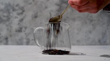 Kurutulmuş siyah çay yapraklarını kaşıkla, cam bir tencereye ekliyorum. Gevşek siyah çay.
