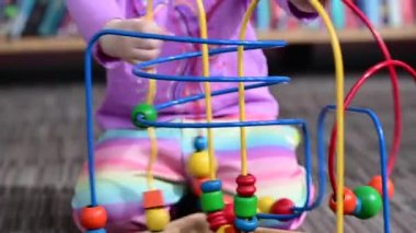 Küçük kız kütüphanede eğitici tahta bir oyuncakla yerde oynuyor, Montessori oyuncağı.