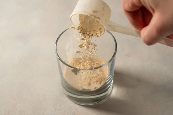 用勺子把蛋白质粉末倒入玻璃杯中 制造蛋白质饮料 — 图库照片