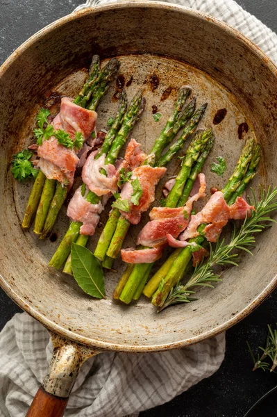 Wrapped asparagus with bacon in frying pan. Dark background