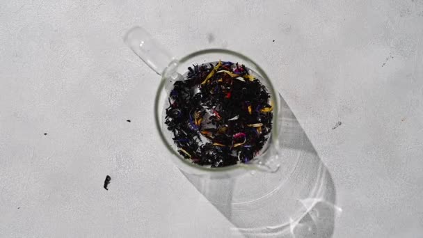 Падение Сушеных Черных Чайных Листьев Сушеными Цветами Стакан Вид Сверху — стоковое видео