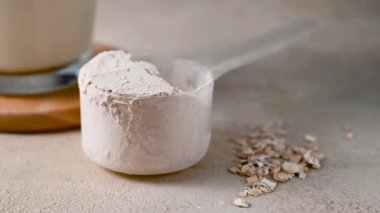 Protein tozu kepçeyle, protein içeceği de arka planda.