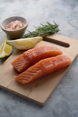 Çiğ somon fileto bifteği, limon ve taze otlarla, gri arka planda.