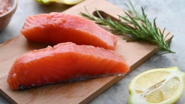 Çiğ somon bifteği, limon ve taze otla birlikte, gri arka planda.