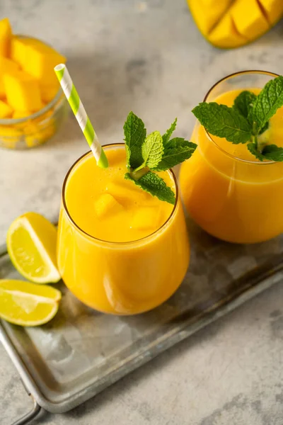 Arka planda taze mango olan bir bardakta mango smoothie. Mango ferahlatıcı içecek.