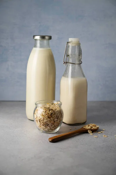 stock image Oat milk in glass bottles with flakes on grey background