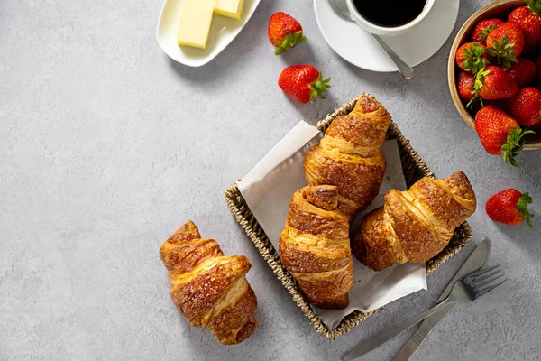 stock image Fresh croissants in a basket for breakfast, with coffee and fresh strawberries, copy space.