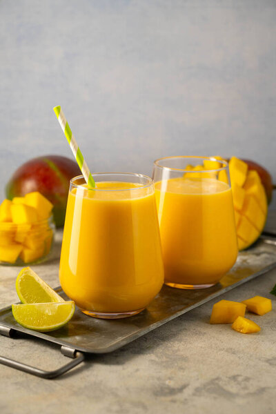 Mango smoothie in a glass with fresh mango on background