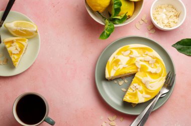 Lemon cheesecake tart or pie, with fresh lemons. Pink background.