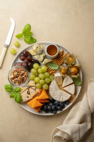 Cheese board, platter with assorted various cheeses, fruits, nuts and snacks. Warm background