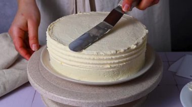 Kadın pandispanya pastasını kremayla şekillendiriyor, pastada beyaz krema var. Ev yapımı.