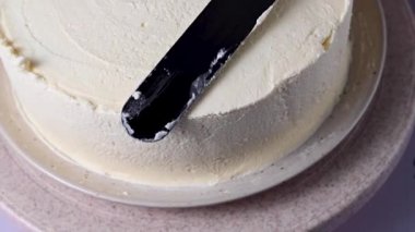 Kadın pandispanya pastasını kremayla şekillendiriyor, pastada beyaz krema var. Ev yapımı.