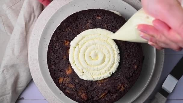 自宅で焼いたチョコレートケーキを飾る スポンジケーキにホイップクリームを配管する女性の手 — ストック動画