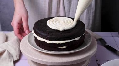 Ev yapımı çikolatalı pasta süslemek. Sünger kekine çırpılmış krema döken kadın eller.