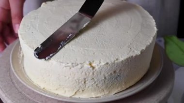 Kadın pandispanya pastasını kremayla şekillendiriyor, pastada beyaz krema var. Ev yapımı.