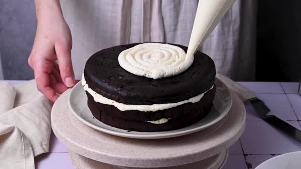 自宅で焼いたチョコレートケーキを飾る スポンジケーキにホイップクリームを配管する女性の手 — ストック動画