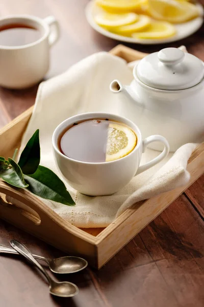 Drinking tea, white ceramic cup and tea pot with black tea and lemon slice
