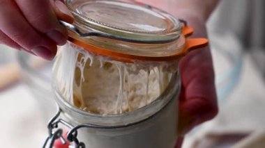 Ekşi hamurlu ekmek kavanozunun içinde, kadın eli bir bardak yabani mayayı açıyor.