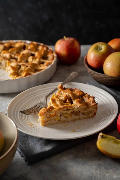 Slice of apple pie, homemade fresh fruit pie with red apples, dark background.