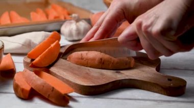 Tatlı patates dilimleri pişirmek, kadın elleri kesme tahtasındaki çiğ patatesleri dilimlemek