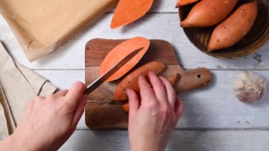 Tatlı patates dilimleri pişirmek, kadın elleri kesme tahtasındaki çiğ patatesleri dilimlemek