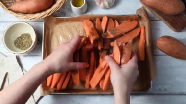 Ev yapımı tatlı patates dilimleri, tabakta patates kızartması. Dişi eller dilimlenmiş patatesleri baharatlarla karıştırıyor.