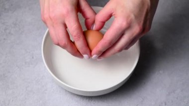 Female hands holding a cracked egg and breaking it. Cooking breakfast or baking. Protein food.