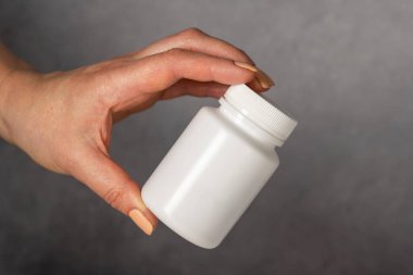 Beyaz plastik bir şişeyi haplarla tutan bir kadın. Kapsüller, kolajen, vitaminler, ağrı kesiciler veya ilaçlar.