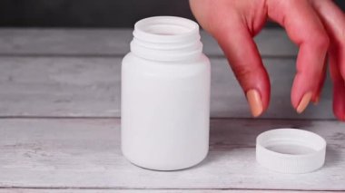 Yiyecek takviyesi, beyaz plastik şişe. Beyaz kapsüller, kolajen, vitaminler, ağrı kesiciler. Kadın elleri.