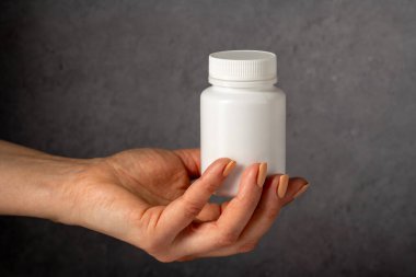Beyaz plastik bir şişeyi haplarla tutan bir kadın. Kapsüller, kolajen, vitaminler, ağrı kesiciler veya ilaçlar.