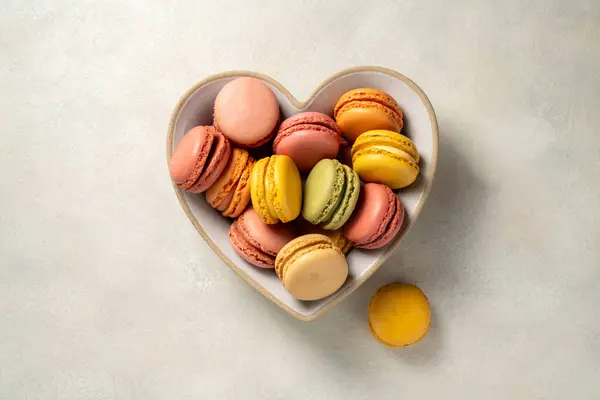 stock image Macarons cookies in heart shaped plate, french macarons on bright background. Gift birth day, Valentines day.