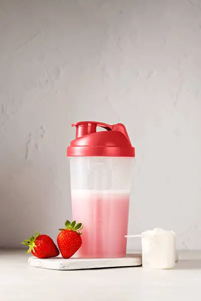 stock image Pink strawberry protein drink shake in a shaker bottle, and protein powder in a scoop.