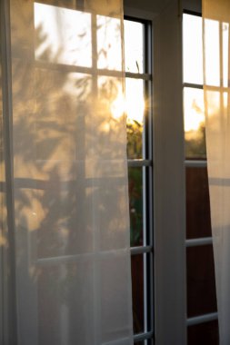 Sonbahar zamanı, penceredeki şeffaf perdelerin arasından gün batımı.