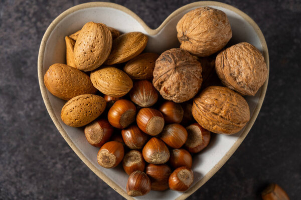 Mix of nuts in a heart shaped bowl, hazelnuts, almonds, walnuts, top view.