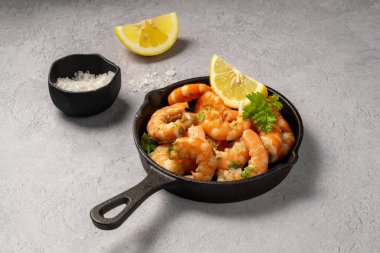 Tavada baharatlı kırmızı karides, taze otlar ve limonla servis edilir..