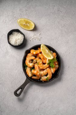 Tavada baharatlı kırmızı karides, taze otlar ve limonla servis edilir..