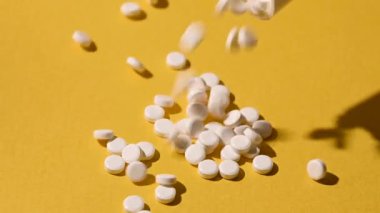 Şeker ikamesi, sarı arka plandan akan tatlandırıcı haplar. Yiyecek takviyesi. Şeker hastası, aşırı kilolu, sağlık konsepti. Ağır çekim, makro çekim..