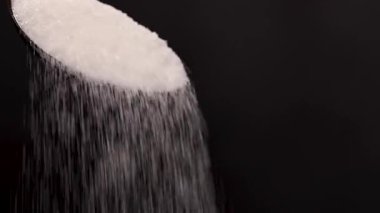 Granüle kamış şekeri düşüyor. Beyaz şekerli kaşık. Siyah arkaplan